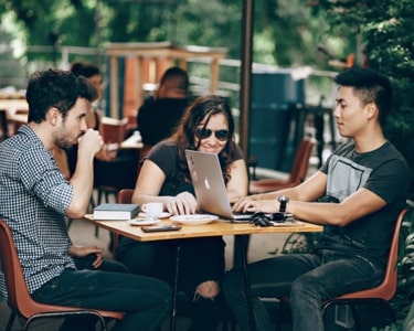 three team members sitting at a cafe and working while enjoying a cup of coffee